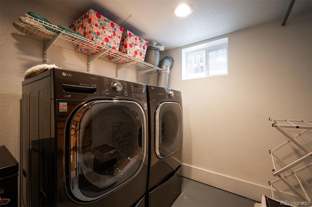 clothes washing area with laundry area, washing machine and dryer, baseboards, and a textured wall