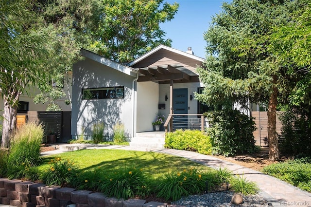 view of front of house with stucco siding, a front yard, and fence