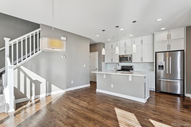 kitchen featuring stainless steel appliances, decorative light fixtures, an island with sink, and backsplash