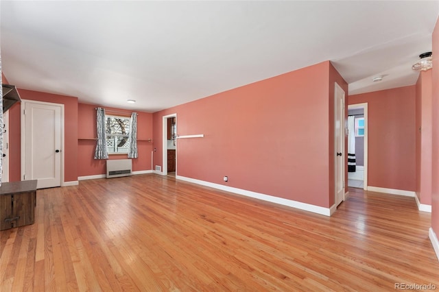 unfurnished living room featuring baseboards, radiator, and light wood-style floors