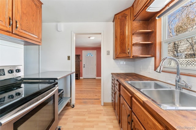 kitchen featuring brown cabinets, decorative backsplash, stainless steel range with electric cooktop, a sink, and wood counters