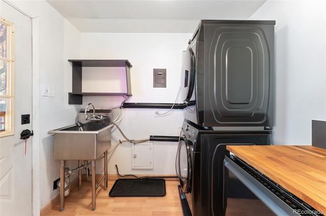 laundry room with light wood finished floors, a sink, stacked washing maching and dryer, laundry area, and electric panel