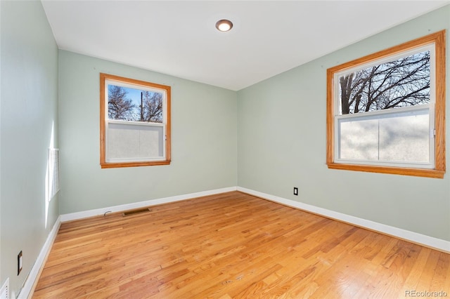 unfurnished room with light wood finished floors, visible vents, and baseboards