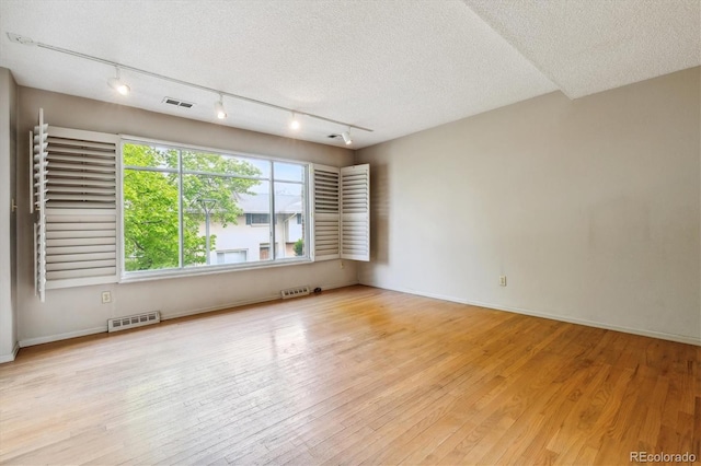 unfurnished room with light hardwood / wood-style floors, a textured ceiling, and track lighting