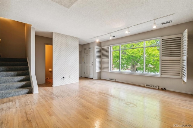 unfurnished living room featuring light hardwood / wood-style floors, a textured ceiling, and rail lighting