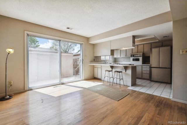 kitchen with white oven, kitchen peninsula, stainless steel refrigerator, light tile flooring, and a kitchen bar