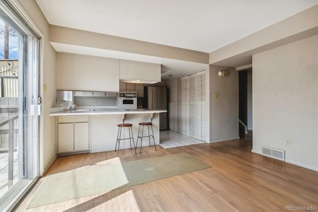 kitchen with kitchen peninsula, stainless steel fridge, white oven, light tile flooring, and a breakfast bar area