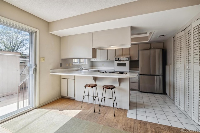 kitchen with white appliances, kitchen peninsula, light tile floors, and a kitchen bar