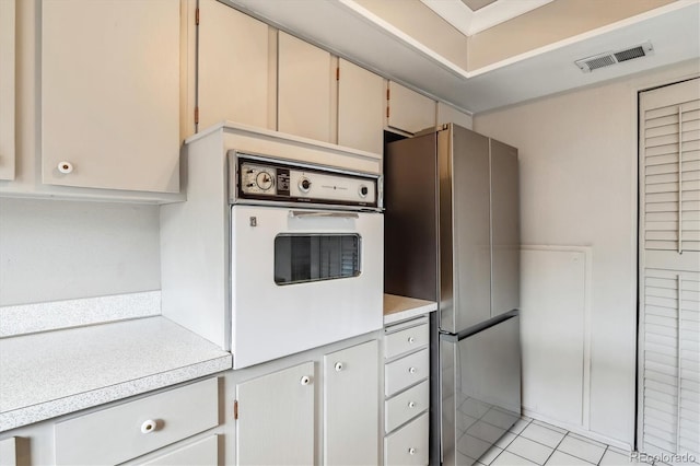 kitchen featuring cream cabinetry, stainless steel fridge, white oven, and light tile floors