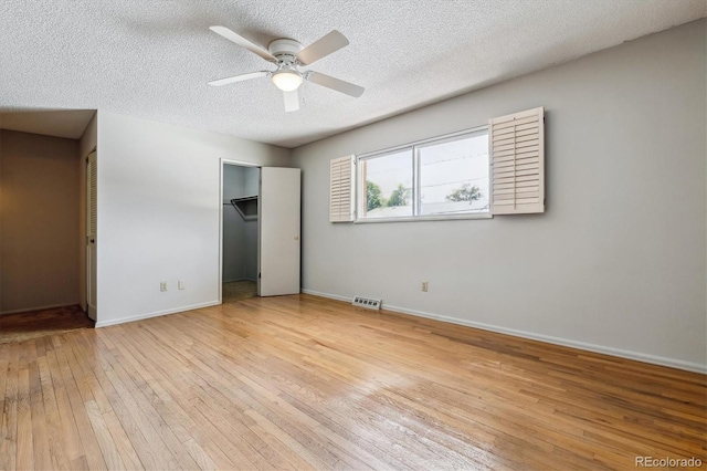 unfurnished bedroom featuring a textured ceiling, a walk in closet, ceiling fan, and light hardwood / wood-style flooring