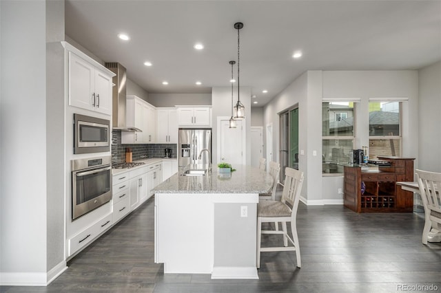 kitchen with decorative backsplash, wall chimney exhaust hood, a breakfast bar, dark wood-type flooring, and stainless steel appliances