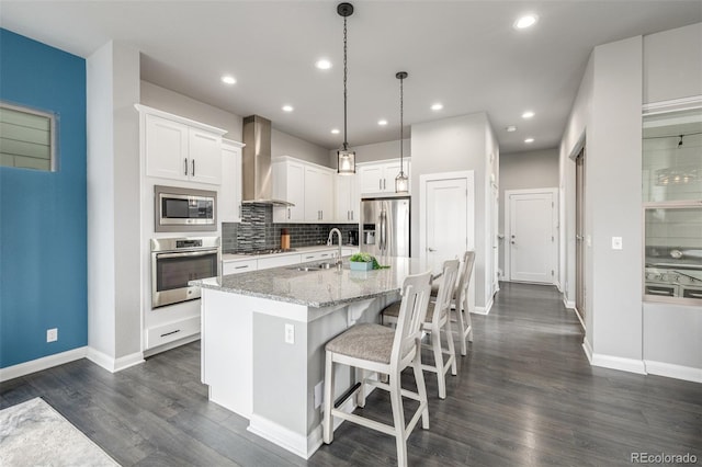 kitchen featuring stainless steel appliances, a sink, backsplash, wall chimney exhaust hood, and dark wood finished floors