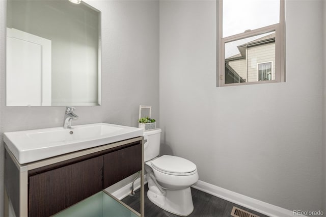 half bathroom with baseboards, visible vents, toilet, wood finished floors, and vanity