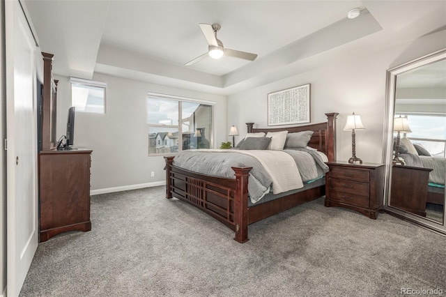 bedroom featuring a ceiling fan, a tray ceiling, baseboards, and carpet