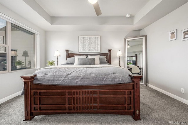 carpeted bedroom featuring ceiling fan, a tray ceiling, and baseboards