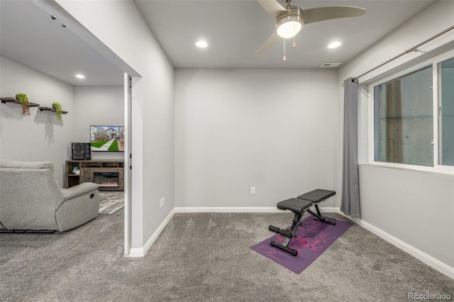 workout area featuring carpet, visible vents, ceiling fan, a warm lit fireplace, and baseboards