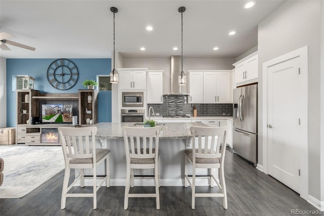 kitchen with white cabinetry, appliances with stainless steel finishes, decorative backsplash, light stone countertops, and wall chimney exhaust hood