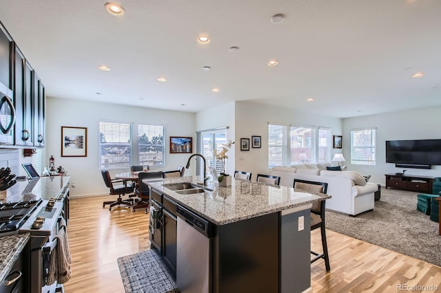 kitchen with light wood finished floors, a kitchen bar, a sink, stainless steel appliances, and light stone countertops