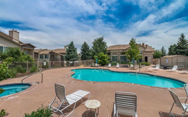 community pool featuring a patio area, a hot tub, a residential view, and fence