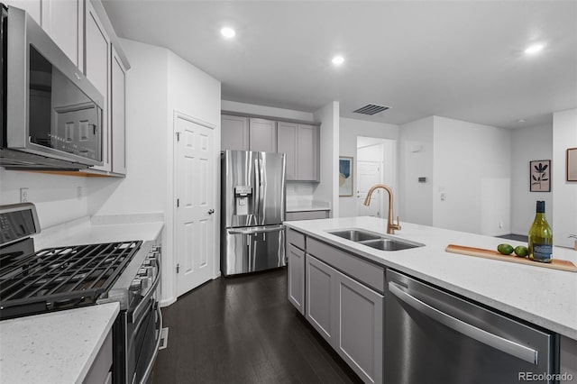 kitchen featuring appliances with stainless steel finishes, a sink, gray cabinets, dark wood finished floors, and recessed lighting