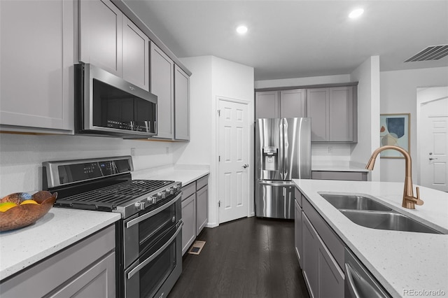 kitchen featuring appliances with stainless steel finishes, gray cabinets, a sink, dark wood-type flooring, and light stone counters