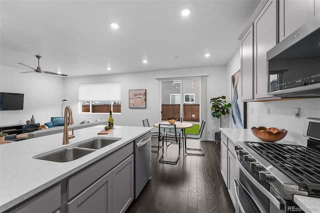 kitchen featuring appliances with stainless steel finishes, a sink, gray cabinetry, dark wood-style flooring, and recessed lighting