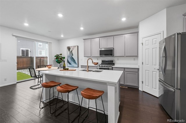 kitchen featuring appliances with stainless steel finishes, gray cabinetry, a sink, dark wood-style floors, and a breakfast bar area