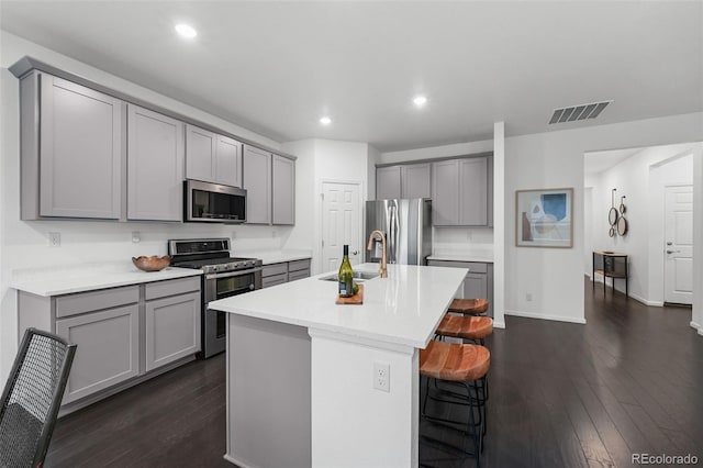 kitchen featuring stainless steel appliances, gray cabinetry, a sink, dark wood-style floors, and a breakfast bar
