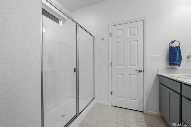 bathroom with a stall shower, tile patterned flooring, baseboards, vanity, and a textured wall