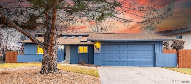 mid-century home with fence, driveway, a shingled roof, a garage, and brick siding