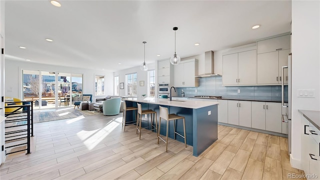 885 Delechant Dr, Erie, CO 80516 - kitchen with white cabinets, an island with sink, hanging light fixtures, stainless steel appliances, and wall chimney range hood