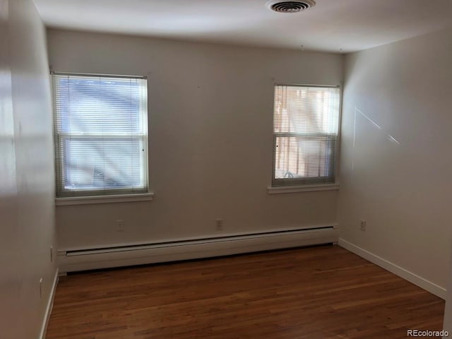 unfurnished room with dark wood-style flooring, baseboard heating, visible vents, and baseboards