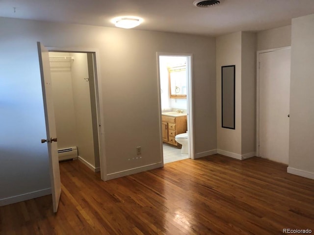 unfurnished bedroom featuring a baseboard heating unit, dark wood-type flooring, a sink, and baseboards