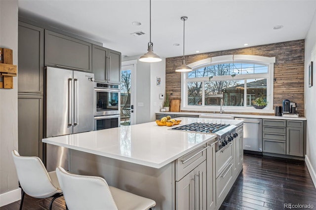 kitchen with dark wood finished floors, stainless steel appliances, gray cabinets, light countertops, and a sink