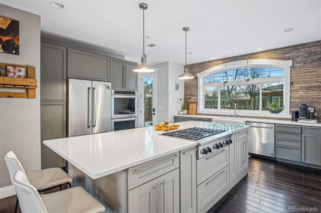 kitchen featuring pendant lighting, dark wood finished floors, stainless steel appliances, gray cabinets, and light countertops