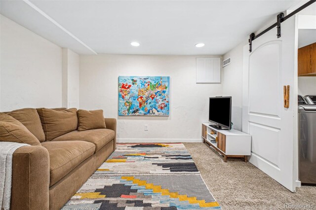 living area with a barn door, light colored carpet, visible vents, baseboards, and washer and clothes dryer