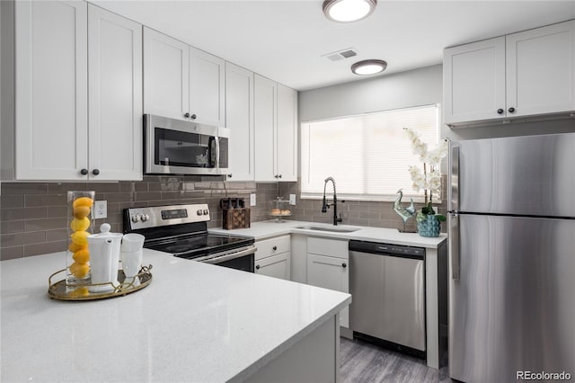 kitchen featuring white cabinets, stainless steel appliances, sink, backsplash, and light hardwood / wood-style flooring