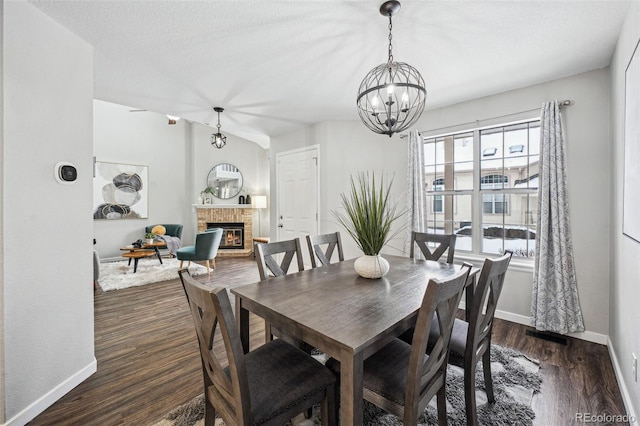 dining area with a healthy amount of sunlight, an inviting chandelier, dark wood-type flooring, and a fireplace