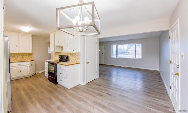 kitchen with stainless steel refrigerator, white cabinetry, black electric range, backsplash, and pendant lighting