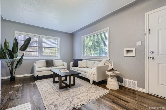 living room with dark wood-style flooring, visible vents, a textured wall, and baseboards