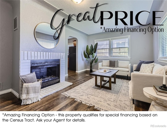 living area with arched walkways, visible vents, a brick fireplace, wood finished floors, and baseboards