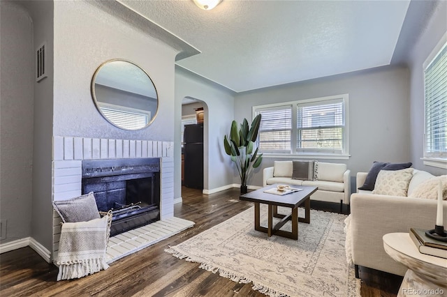 living room with baseboards, arched walkways, wood finished floors, a textured ceiling, and a fireplace