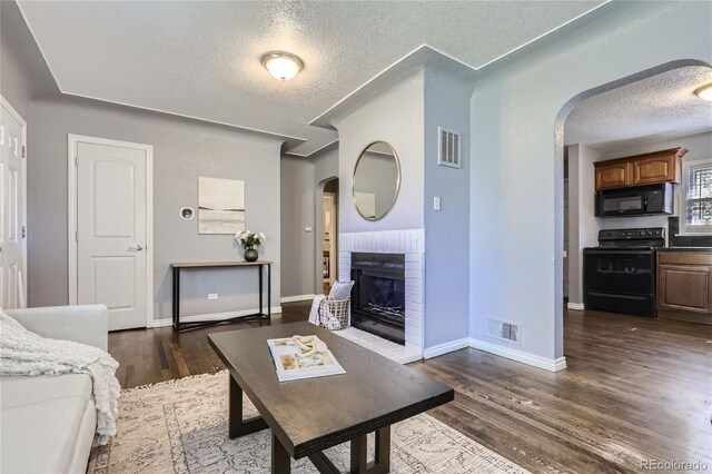 living area with dark wood-style floors, a fireplace, arched walkways, and visible vents