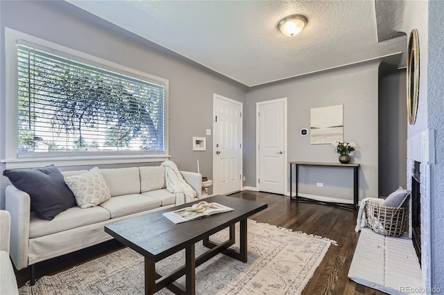 living room with dark wood-style flooring, a textured ceiling, and baseboards