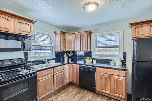 kitchen with a textured ceiling, a sink, backsplash, black appliances, and light wood finished floors