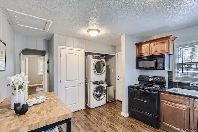 kitchen featuring arched walkways, dark wood-style flooring, stacked washer / drying machine, black appliances, and a sink