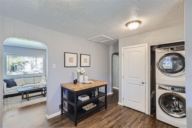 clothes washing area with attic access, stacked washer / dryer, dark wood finished floors, and arched walkways