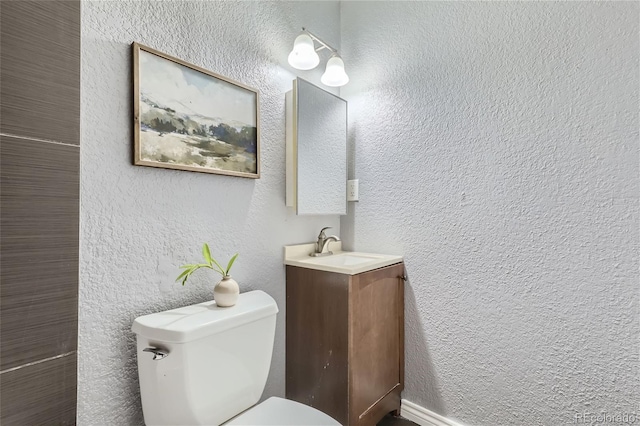 half bathroom with toilet, vanity, and a textured wall