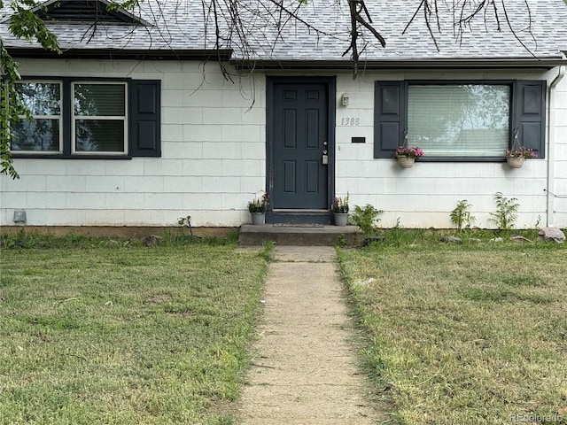 entrance to property with roof with shingles and a lawn