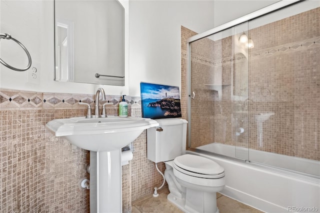 bathroom with tile patterned floors, toilet, shower / bath combination with glass door, and tile walls